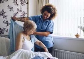 Home Caregiver helping a senior woman get dressed in her bedroom.