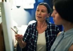 Portrait of mature woman professor helping student to draw, discussing work and explaining mistakes